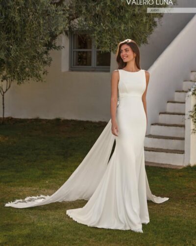 Sensual vestido de novia confeccionado en crepe de corte sirena. combinado con encaje y pedrería. Muestra un escote barco en el delantero con un corte imperio que estiliza la figura. La espalda abierta ilusión con aplicaciones de encaje y los tirantes que se ciñen en la cintura desde donde parte una sobrecola espectacular de georgette y encaje. hacen de este traje un diseño de ensueño. ideal para cualquier ceremonia.