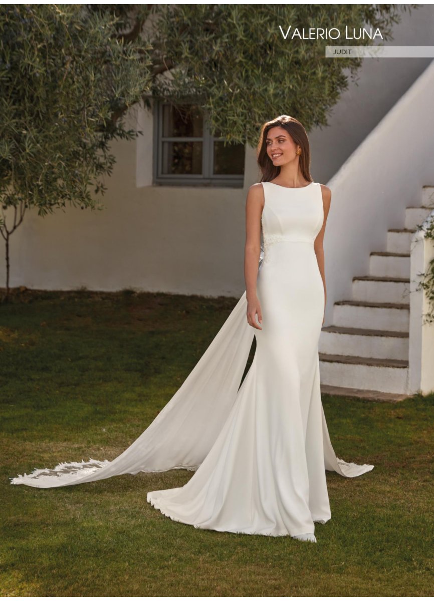Sensual vestido de novia confeccionado en crepe de corte sirena. combinado con encaje y pedrería. Muestra un escote barco en el delantero con un corte imperio que estiliza la figura. La espalda abierta ilusión con aplicaciones de encaje y los tirantes que se ciñen en la cintura desde donde parte una sobrecola espectacular de georgette y encaje. hacen de este traje un diseño de ensueño. ideal para cualquier ceremonia.