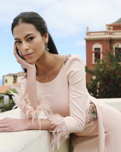 El vestido de fiesta Nala irradia elegancia y feminidad en cada detalle. Confeccionado en crepe fluido, este diseño largo destaca por su drapeado en la cintura, que realza la silueta de forma sutil y favorecedora. Los apliques joya en el hombro y el costado aportan un brillo delicado, mientras que las mangas con plumas añaden un toque sofisticado y actual. Este vestido combina estructura, movimiento y luz en un mismo diseño. Una opción ideal para mujeres que buscan un vestido de fiesta elegante con detalles únicos y un estilo atemporal.