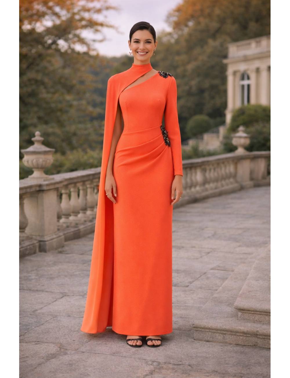 Vestido largo de corte recto y silueta estilizada que destaca por su elegancia atemporal. Presenta original escote asimétrico con cuello alto, manga larga y una delicada capa lateral que aporta movimiento y sofisticación. El detalle joya en el hombro añade un toque exclusivo. Ideal para eventos, bodas, graduaciones o celebraciones especiales donde quieras brillar con clase.