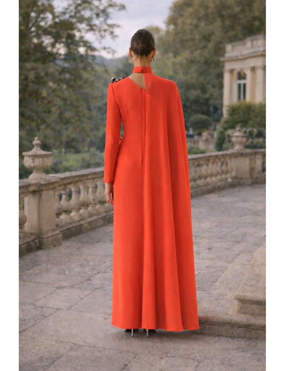 Vestido largo de corte recto y silueta estilizada que destaca por su elegancia atemporal. Presenta original escote asimétrico con cuello alto, manga larga y una delicada capa lateral que aporta movimiento y sofisticación. El detalle joya en el hombro añade un toque exclusivo. Ideal para eventos, bodas, graduaciones o celebraciones especiales donde quieras brillar con clase.